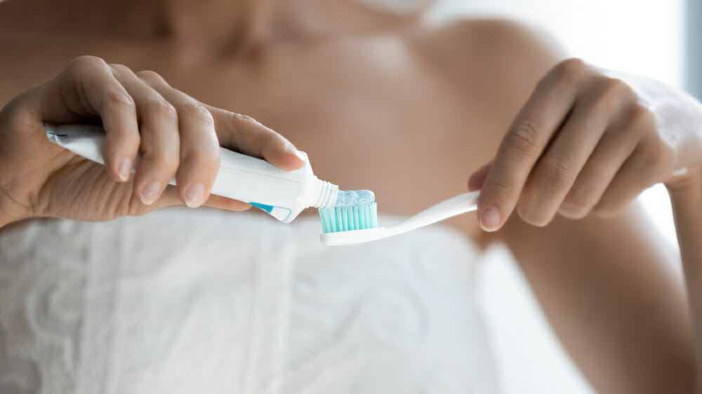 Toothpaste being applied to toothbrush by woman in towel